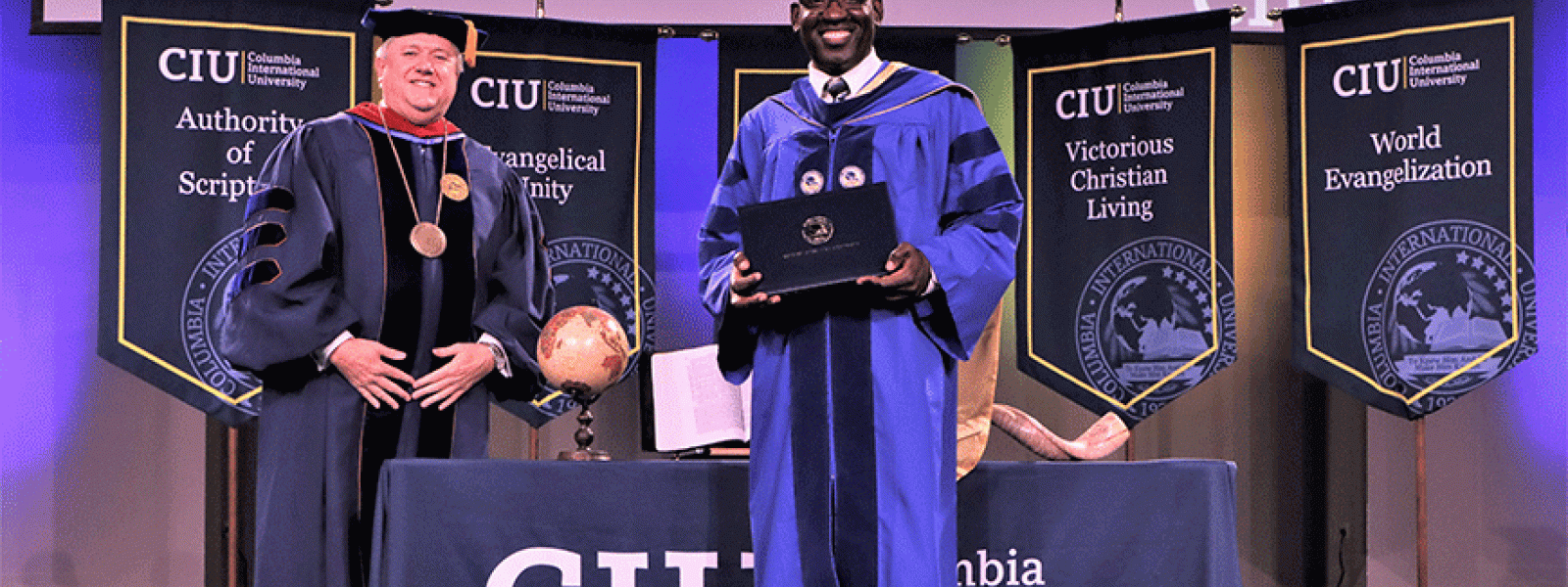 Keeping social distance, CIU President Mark Smith poses with graduate Patrick Gue who earned a Ph.D. in Intercultural Studies. Gue is originally from Haiti and pastors a church in South Carolina.