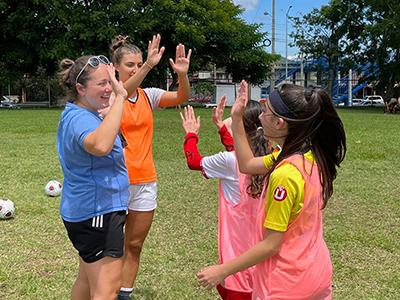 Head Coach Kara Farnsworth Lail (left) shares high fives at a soccer clinic. 