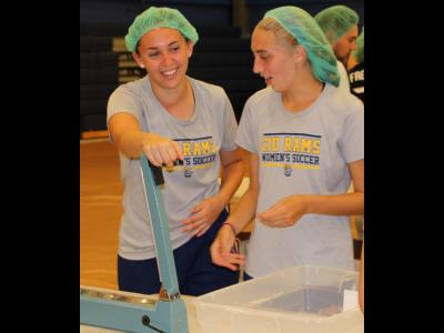 Women's soccer players Meghan Esquinaldo (left) and Taylor Endicott share a laugh as they wait to seal another bag of lentil casserole.